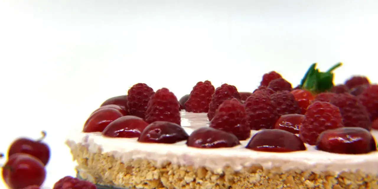 Cheesecake senza gelatina, guarnita con lamponi succosi e ciliegie lucide, su una base croccante.