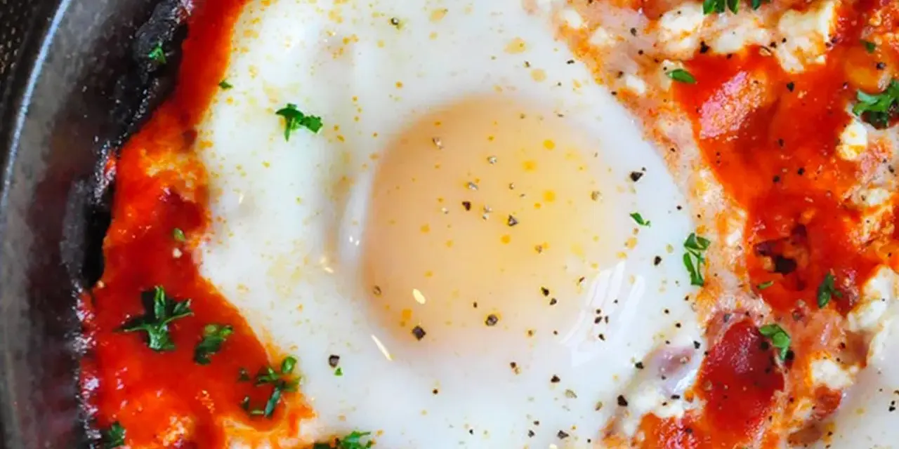 Uova al pomodoro, un piatto saporito con uovo cotto in salsa di pomodoro e formaggio, guarnito con prezzemolo fresco.