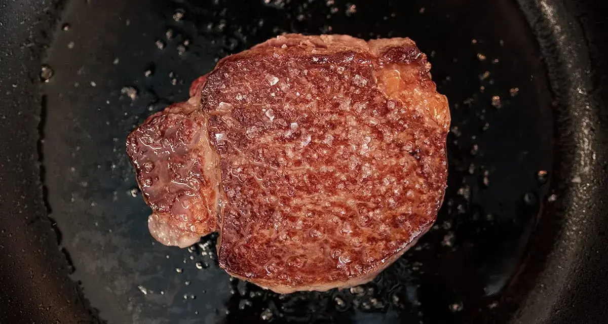 Ein saftiges Steak brutzelt in der Pfanne, bestreut mit grobem Salz.