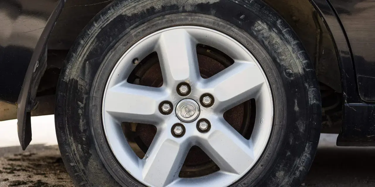 Ruota sgonfia dell'auto, con cerchione in lega a cinque razze e pneumatico sporco.
