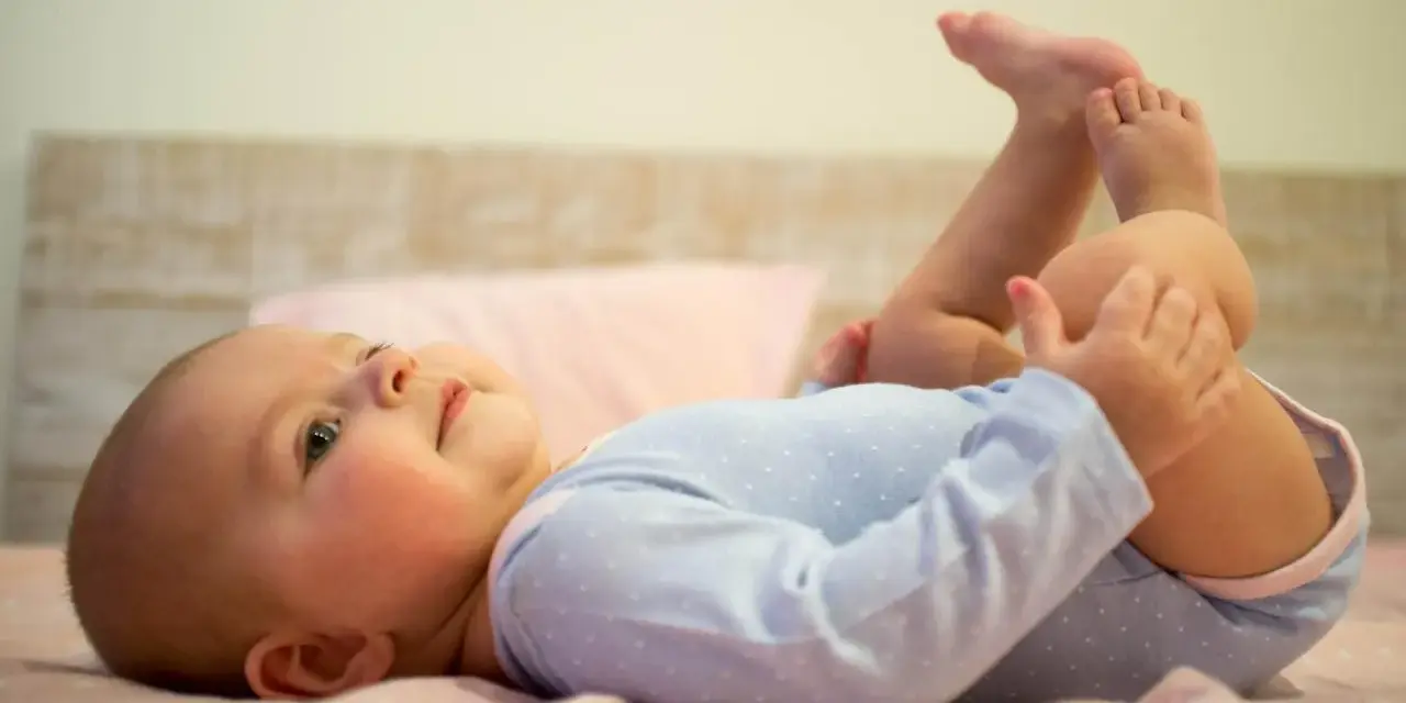 Uśmiechnięte, 5 miesięczne dziecko leży na plecach, podnosząc nóżki do góry.