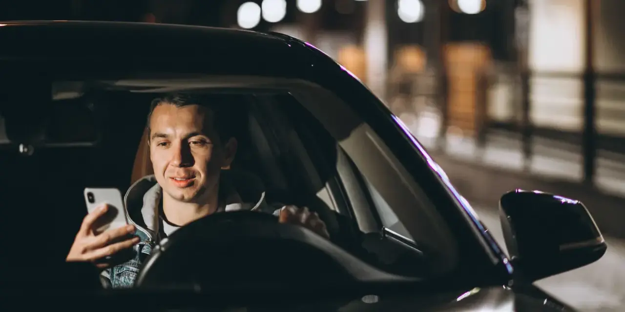Mężczyzna w samochodzie Uber Black sprawdza telefon, planując trasę i licząc na dobre uber black zarobki.