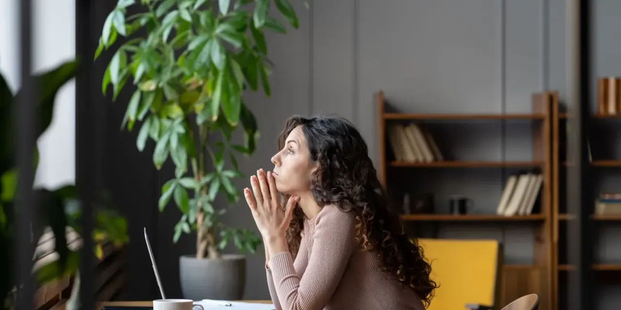 Mujer pensativa en su escritorio, con las manos juntas, reflexionando sobre sus permisos retribuidos.