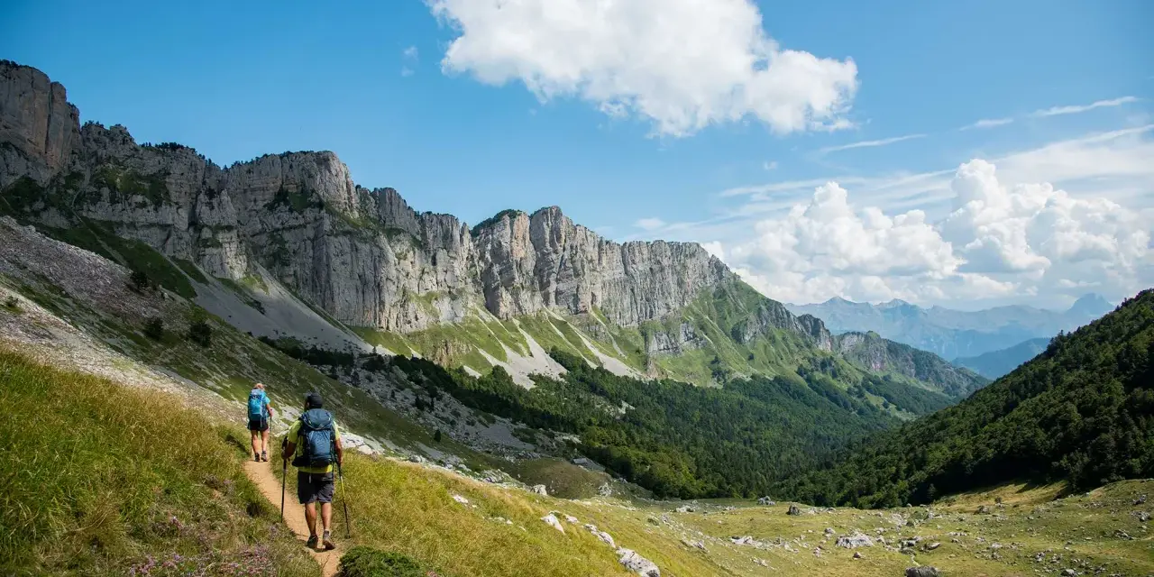 Deux randonneurs explorent un sentier escarpé au Pays Basque, sous un ciel bleu et des falaises imposantes.