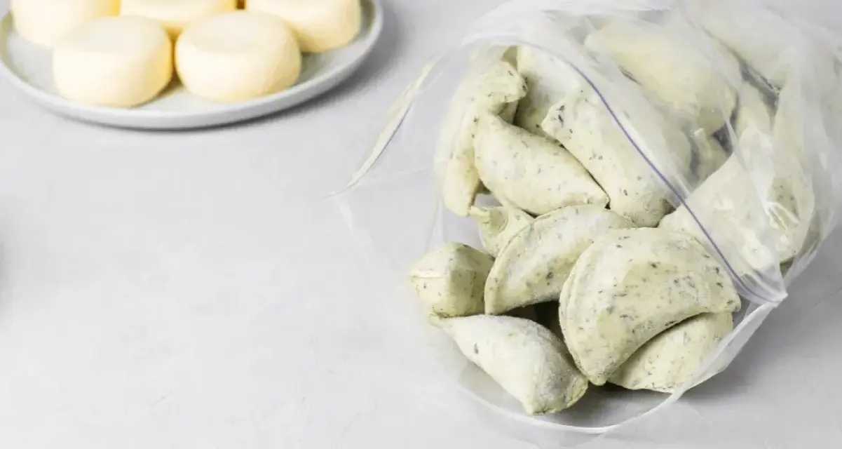 Mrożone pierogi w woreczku obok talerza z okrągłymi serkami.