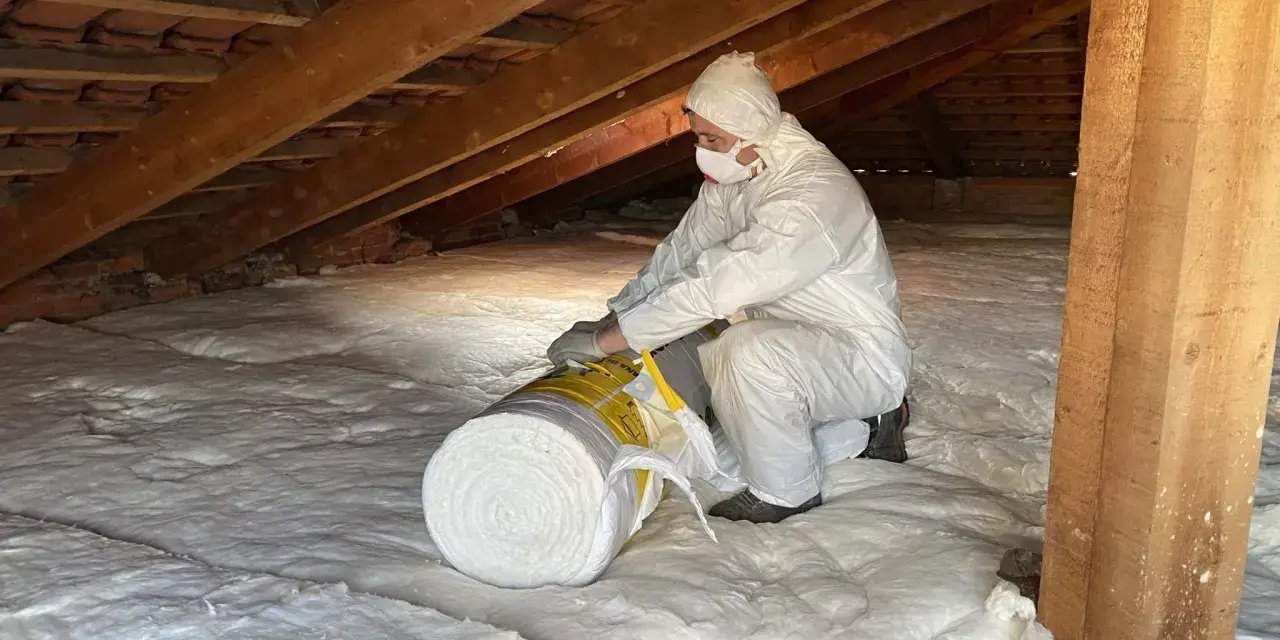 Persona in tuta protettiva posiziona un rotolo di lana di roccia per isolare il sottotetto.