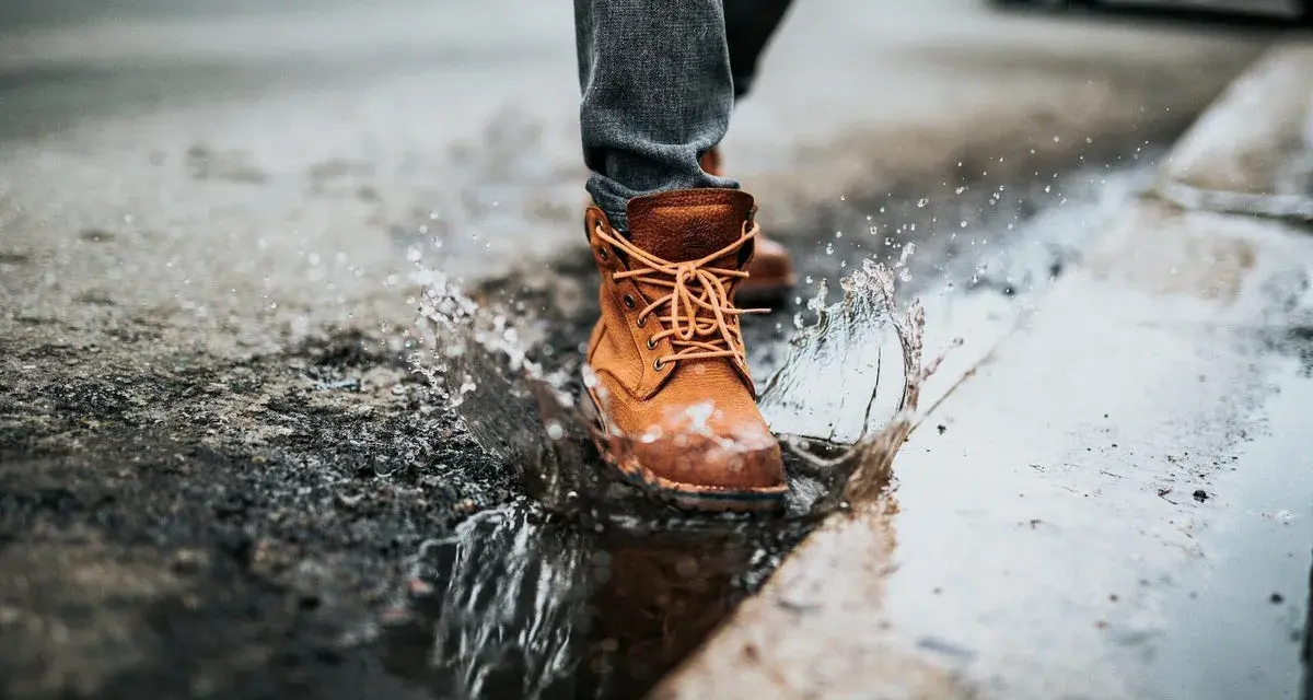 Botas de cuero marrón salpican un charco, demostrando que el cuero es impermeable.