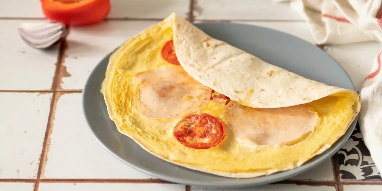 Pyszna tortilla z jajkiem, pomidorem i szynką, gotowa do zjedzenia.