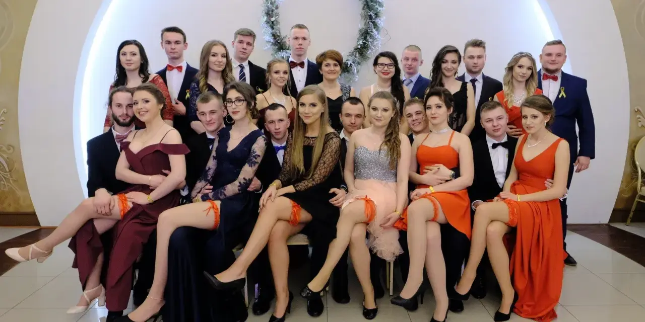 Uczniowie na studniówce, dziewczyny w sukniach, a jedna z nich ma widoczne czerwone majtki na studniówkę.
