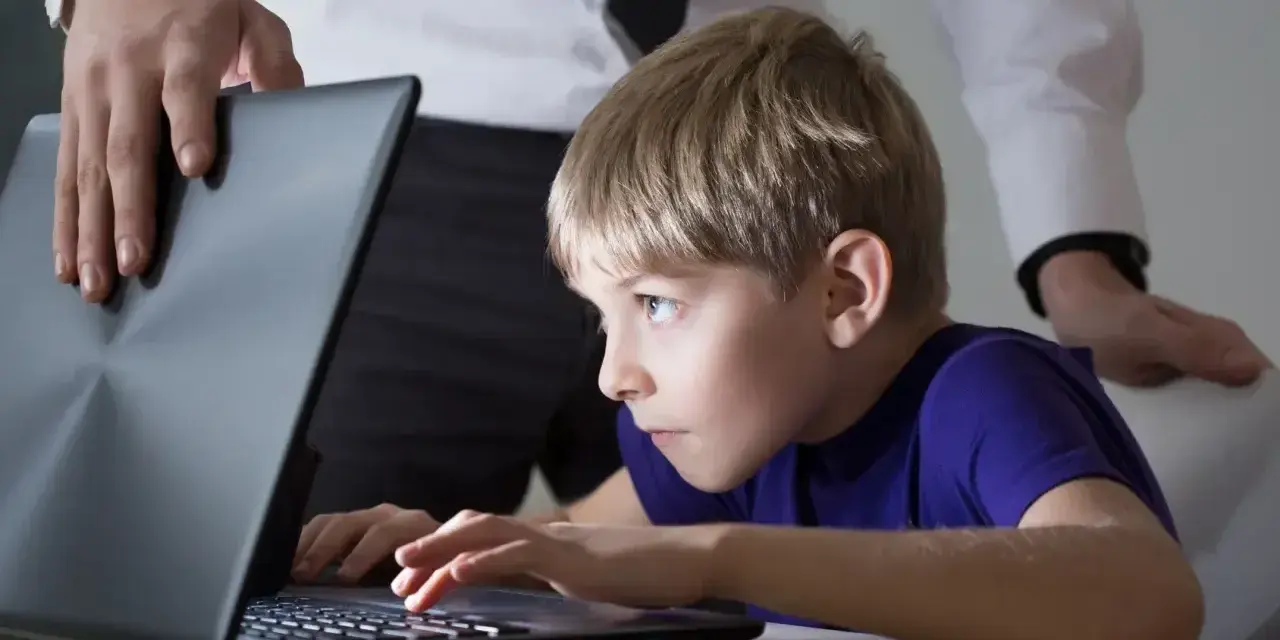 Chłopiec pochłonięty grą na laptopie, a dorosły próbuje pomóc w leczeniu uzależnienia od komputera.