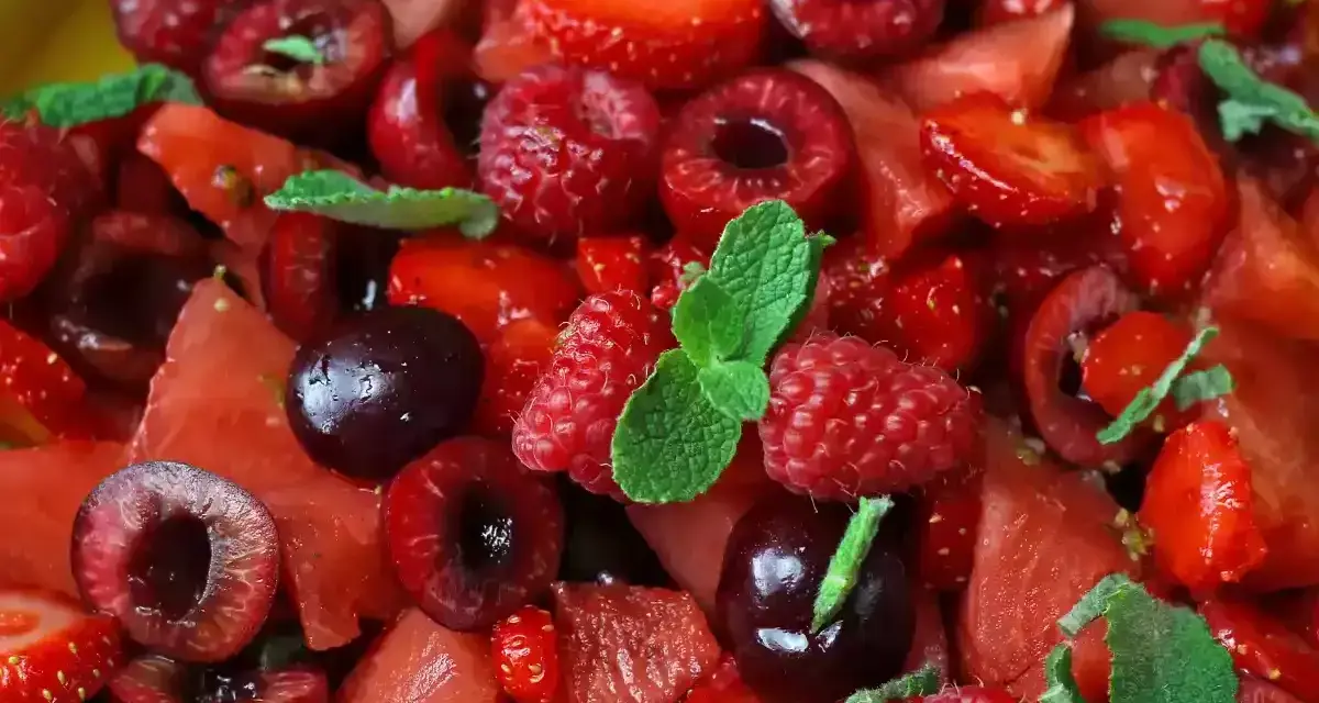 Macedonia di frutta fresca e colorata: fragole, ciliegie, lamponi e anguria, guarnita con foglie di menta.