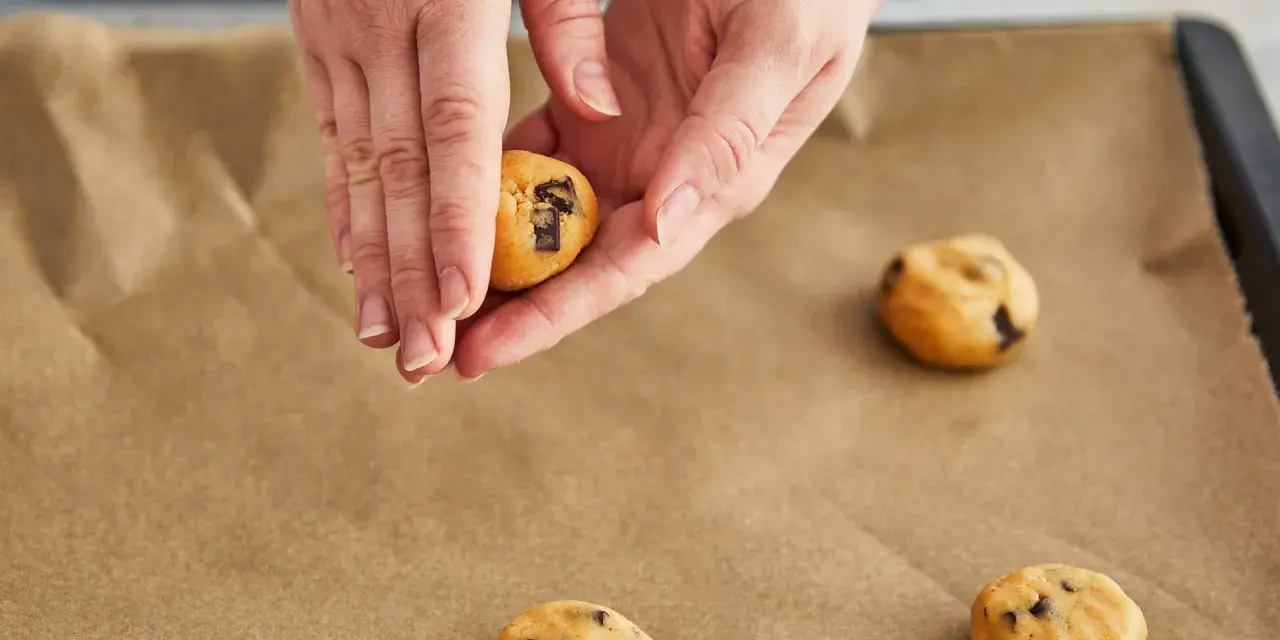 Hände formen Teig für einen Skillet Cookie mit Schokoladenstückchen auf Backpapier.