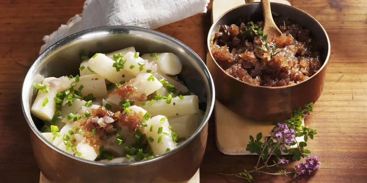 Ein köstliches Haferwurzel Rezept mit karamellisierten Zwiebeln und frischem Schnittlauch. Serviert in Kupfer- und Edelstahlschalen auf einem Holztisch.