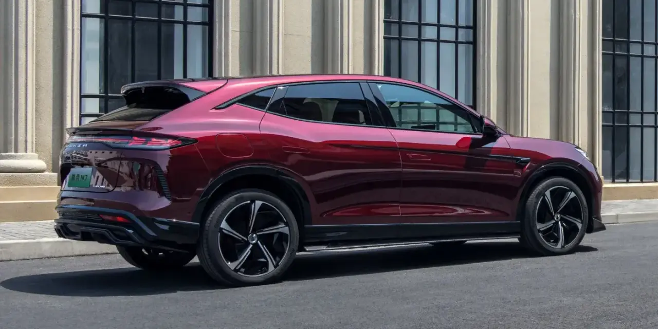 Czerwony luksusowy SUV Denza N9 widziany z boku, na tle budynku z kolumnami.
