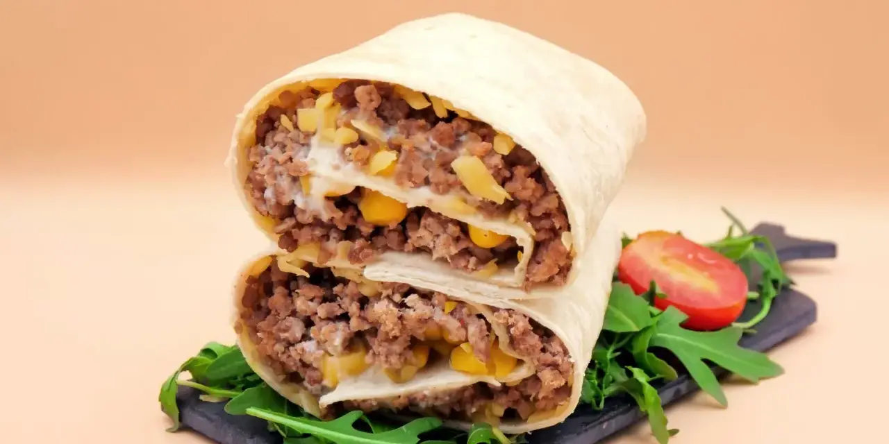 Pyszna tortilla z mięsem mielonym, kukurydzą i serem, przekrojona na pół, z rukolą i pomidorkiem.