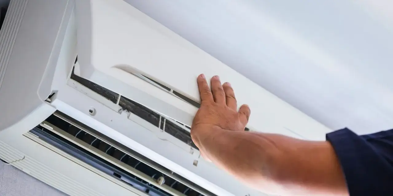 Ręka technika otwiera obudowę klimatyzatora do sprawdzenia szczelności.