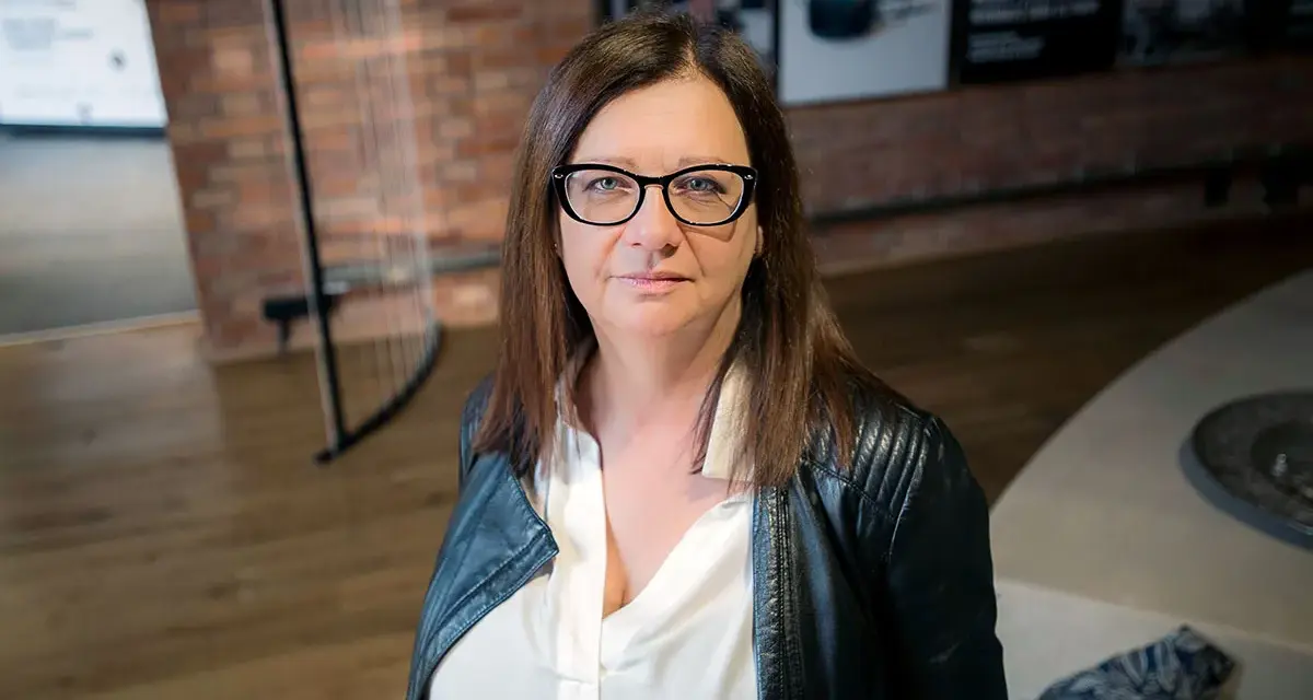 Małgorzata Szczęśniak w okularach i czarnej ramonesce, zamyślona.