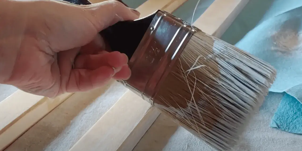 Mano aplica pintura con un pincel seco sobre listones de madera.