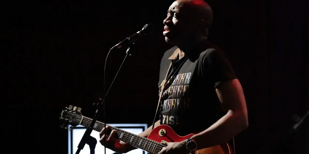 Musiker mit Gitarre und Mikrofon, trägt T-Shirt mit dem Titel von Otis Redding.