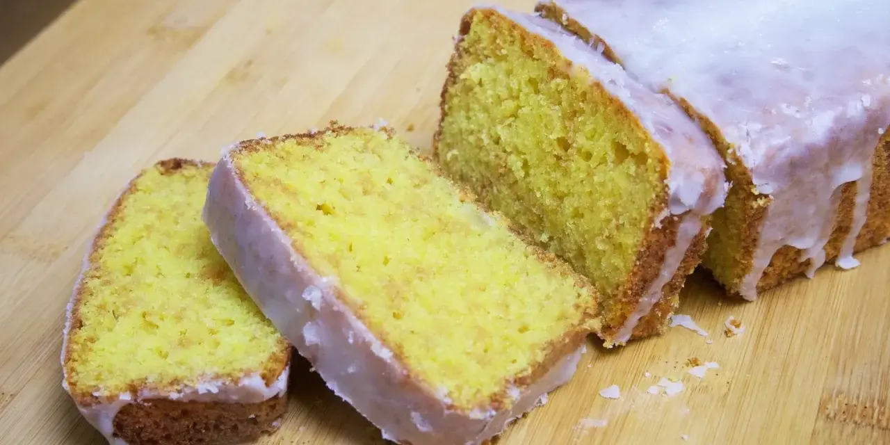 Un delicioso pastel de limón, cubierto con glaseado blanco, cortado en rebanadas sobre una tabla de madera.