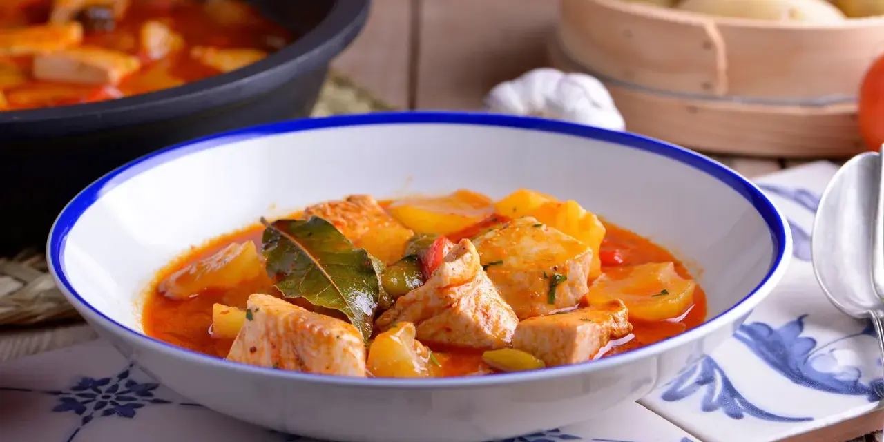Bol de patatas con bonito en salsa roja, decorado con hojas de laurel.