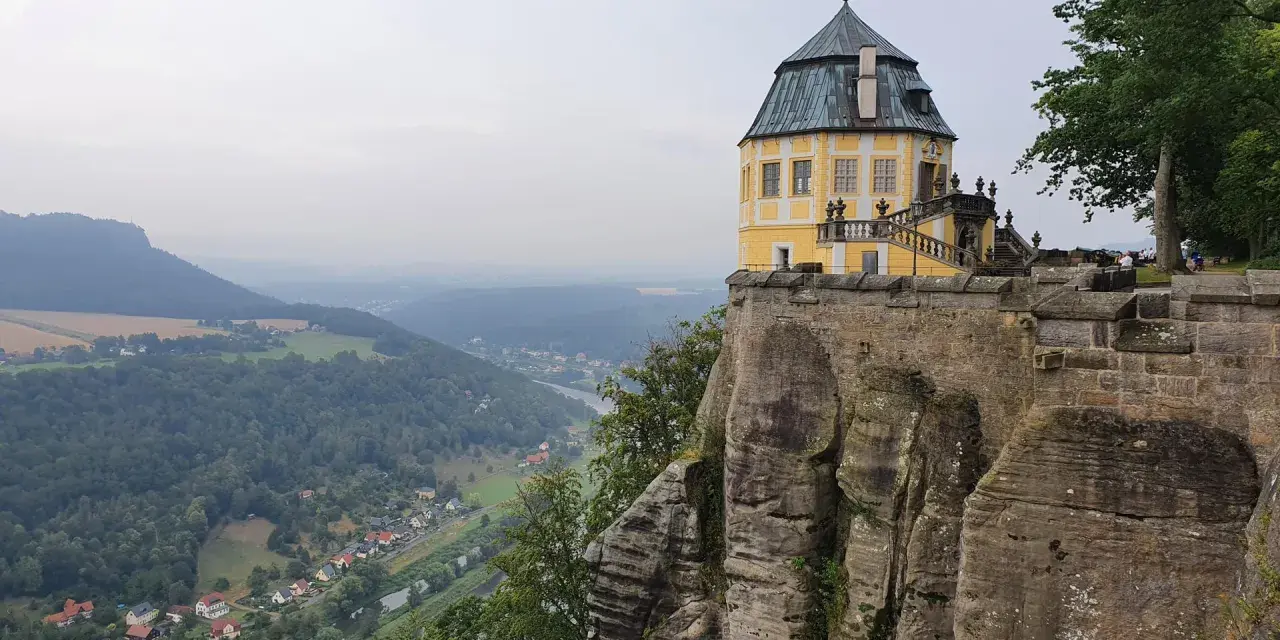 Żółty pałac na skale, część twierdzy Königstein, góruje nad doliną rzeki i lasami.