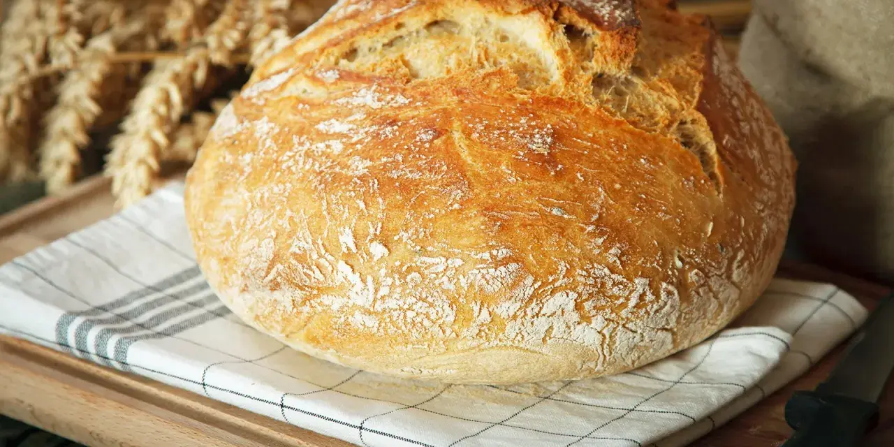 Ein knuspriges, schnelles Brot mit Backpulver, das auf einem karierten Tuch liegt. Im Hintergrund sind Ähren und ein Sack zu sehen.