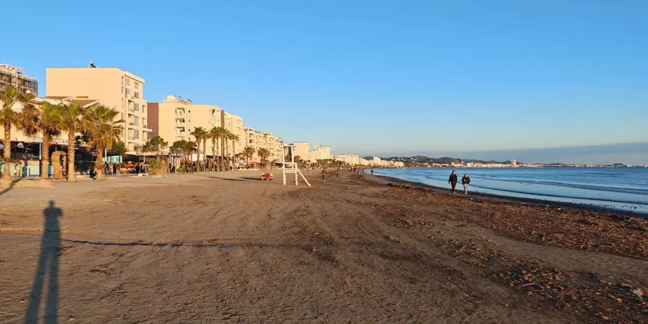 Plaża w Albanii, z palmami i budynkami w tle, idealna na spacer. Klimat sprzyja relaksowi nad morzem.