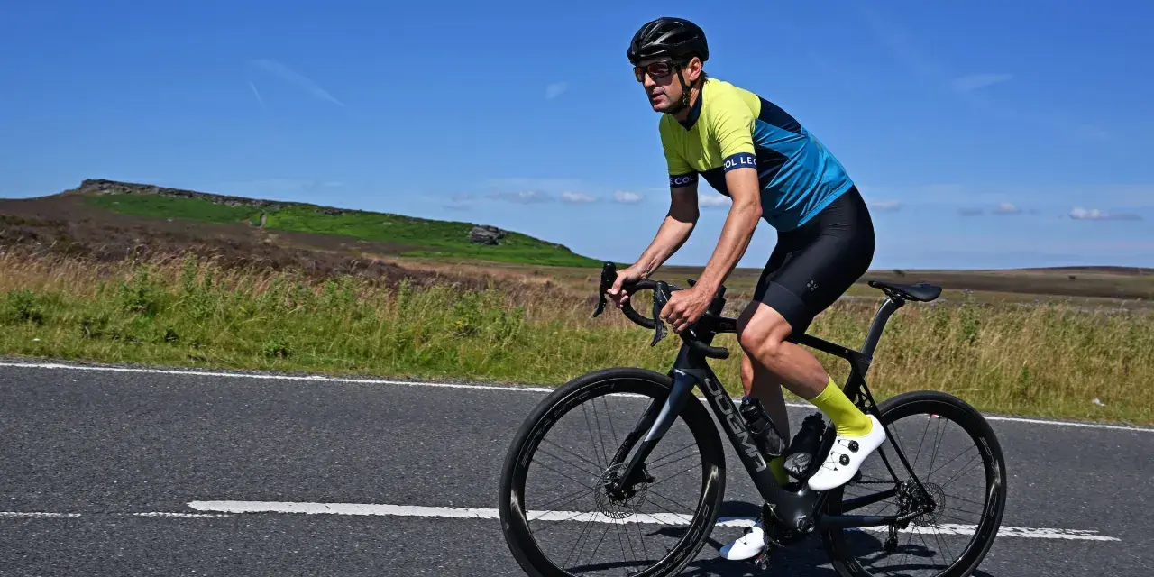 Man cycling on max speed on a scenic road with hills in the background.