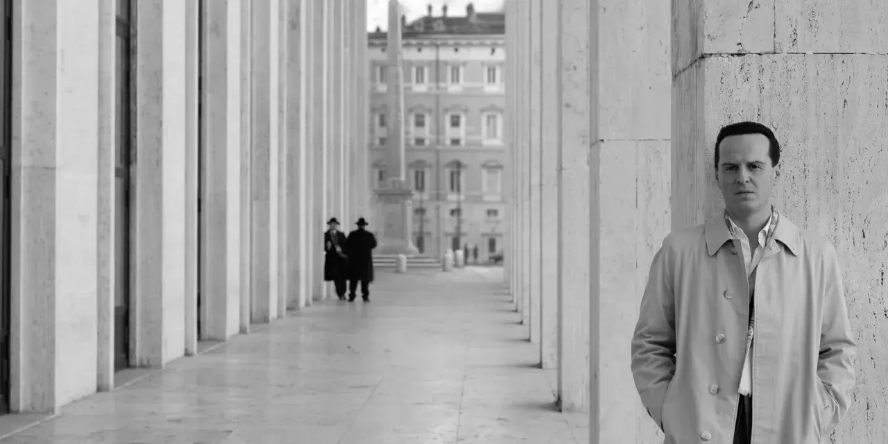 Un uomo in trench osserva l'obiettivo, mentre sullo sfondo due figure in abito scuro passeggiano sotto un colonnato. Potrebbe essere una scena da "Il talento di Mr. Ripley dove è stato girato".