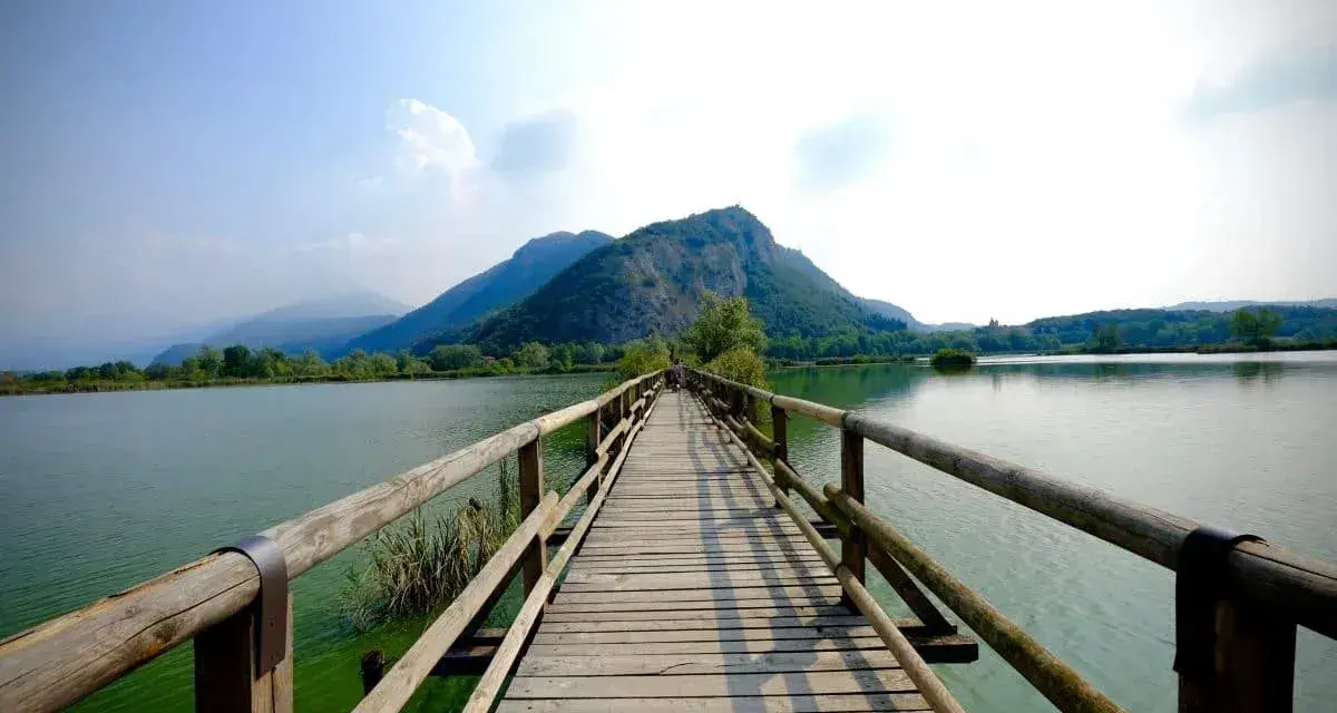 Ponte in legno su lago calmo, montagne verdi sullo sfondo. Un luogo incantevole per scoprire cosa vedere in Franciacorta, tra natura e tranquillità.
