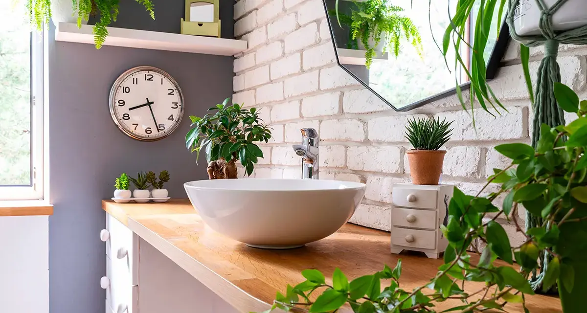 Comment décorer une salle de bain : un lavabo rond sur un meuble en bois, entouré de plantes vertes luxuriantes et d'un miroir mural.