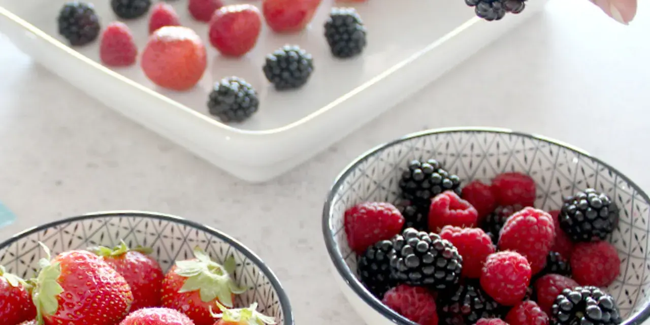 Frische Beeren, darunter Erdbeeren, Himbeeren und Brombeeren, werden für die Lagerung vorbereitet. Man kann Erdbeeren einfrieren, um sie später zu genießen.