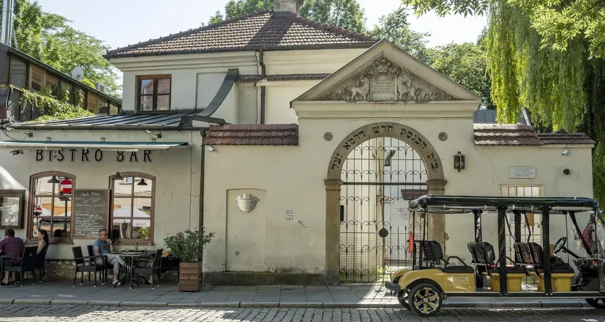 Bistro Bar obok bramy z hebrajskimi napisami, charakterystycznej dla krakowskiej dzielnicy żydowskiej. Obok stoi żółty meleks.