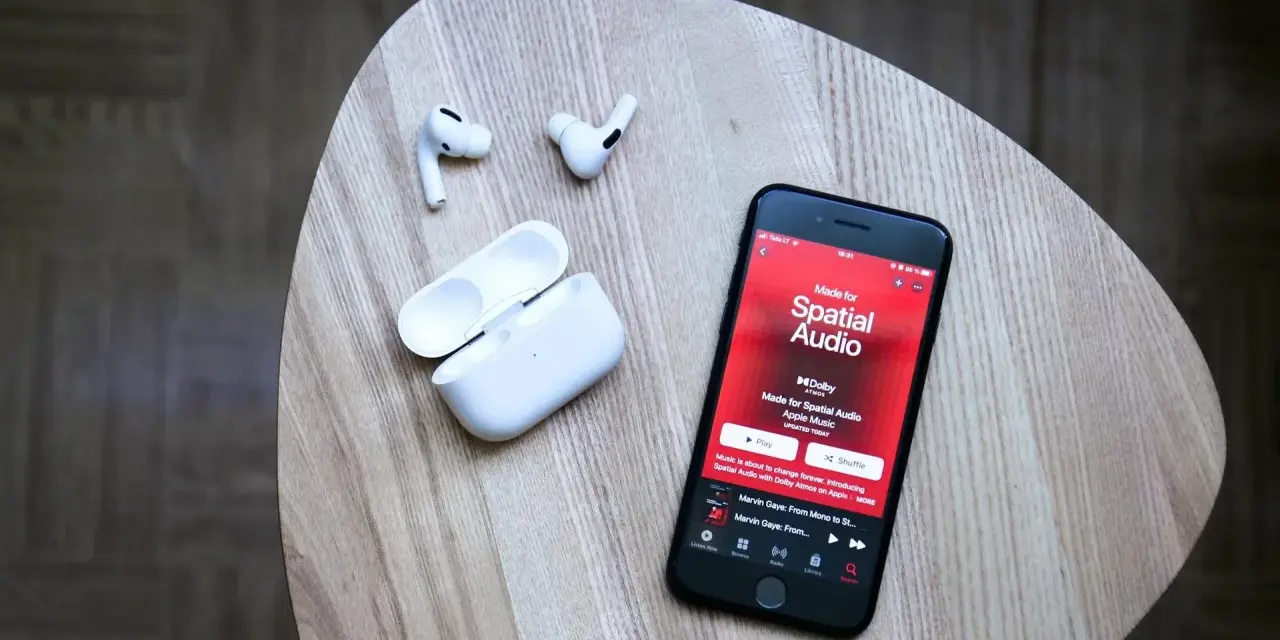 iPhone mit Apple Music Update zeigt "Made for Spatial Audio". AirPods und Ladecase liegen daneben.