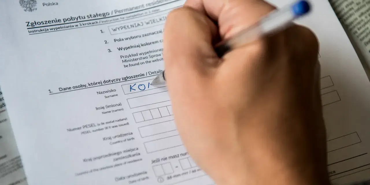 Ręka wypełnia formularz "Zgłoszenie pobytu stałego". Czy jest obowiązek meldunku? Tak, ten dokument to potwierdza.