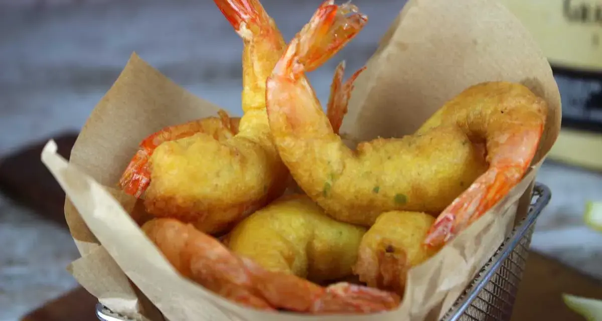 Crujientes gambas a la gabardina doradas y sabrosas, servidas en una cesta metálica con papel de cocina.