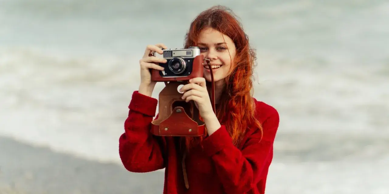 Ruda dziewczyna z aparatem, jak znani fotografowie, uwiecznia piękno morza.
