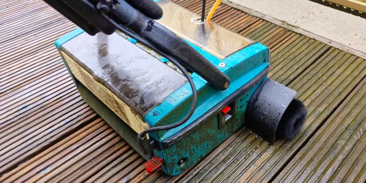 Gerät zur Bankirai Terrasse reinigen mit Bürstenaufsatz auf nassen Holzbrettern.