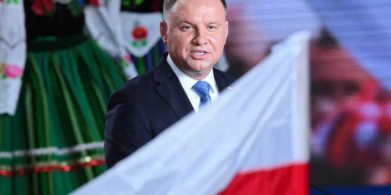 Prezydent Andrzej Duda w garniturze i krawacie, na tle polskiej flagi i tradycyjnego stroju. Ile trwa ułaskawienie prezydenta?