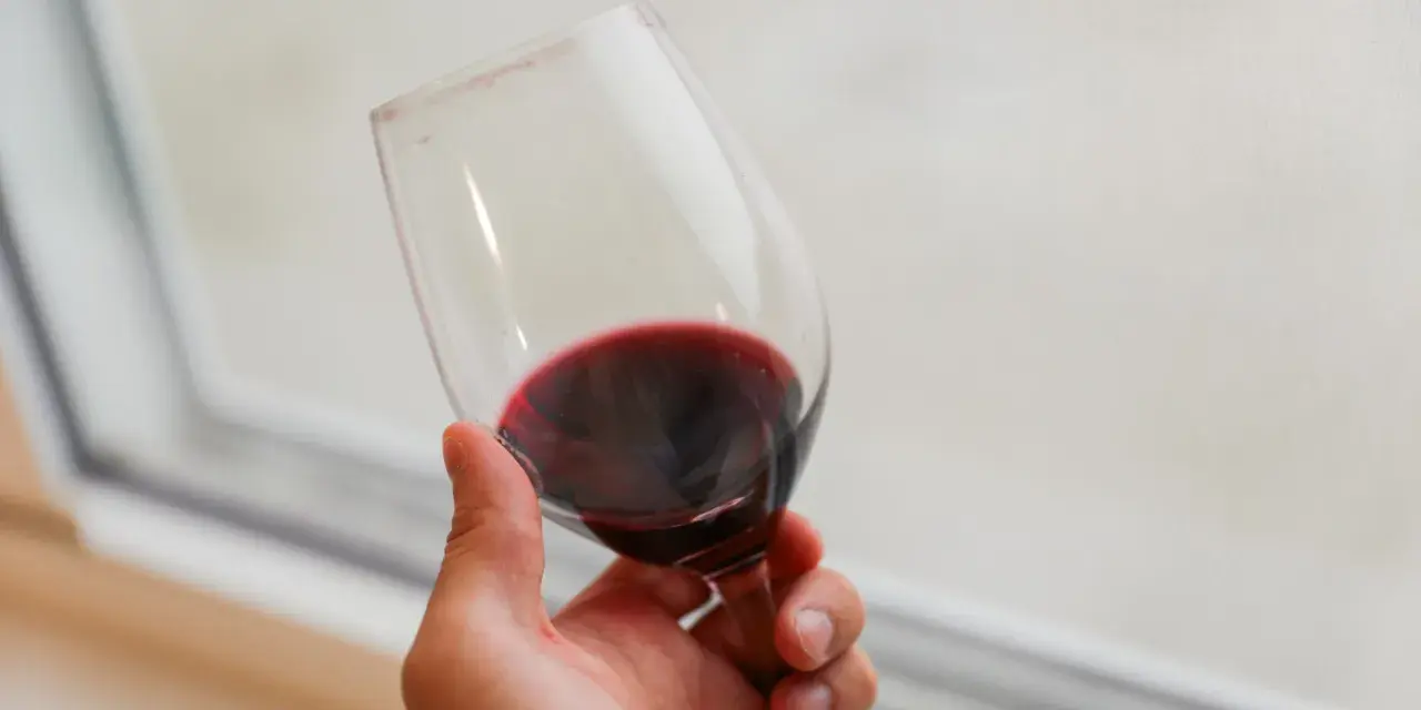 Dłoń trzyma kieliszek czerwonego wina. Czy wino jest zdrowe? To pytanie nurtuje wielu miłośników tego trunku.
