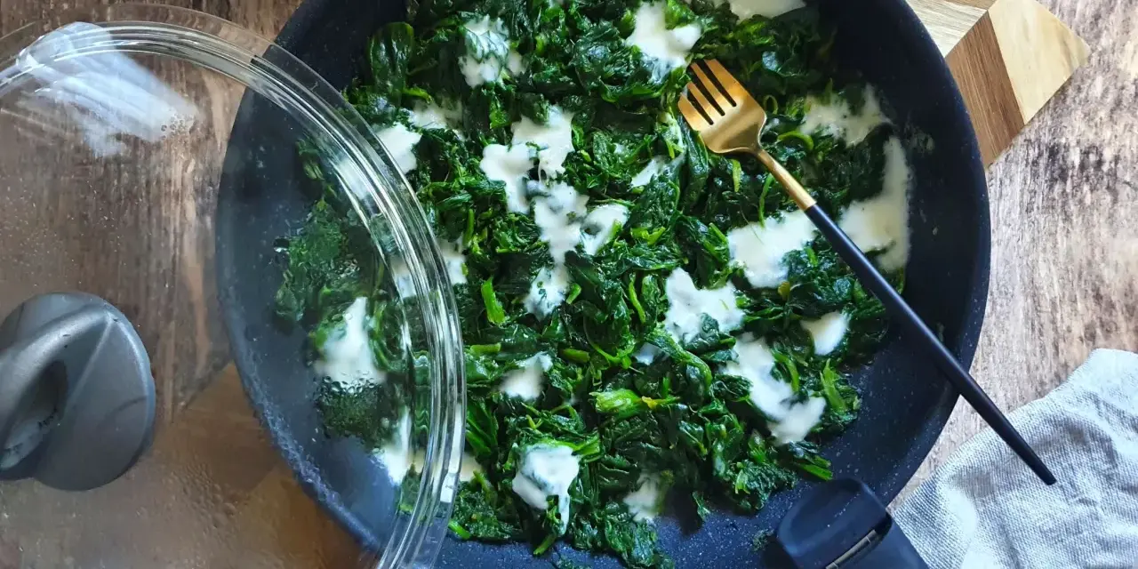 Spinaci in padella cremosi, con una forchetta dorata pronta ad assaggiarli. Un contorno semplice e gustoso.