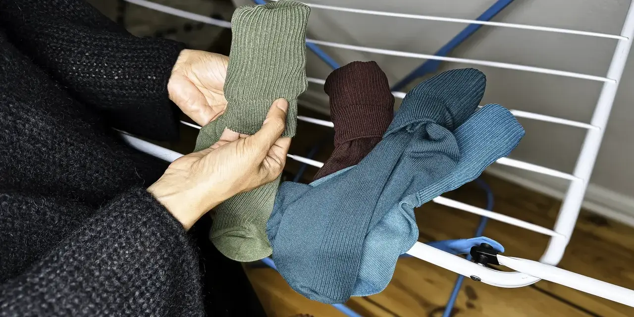 Hände sortieren frisch gewaschene, bunte Socken auf einem Wäscheständer.