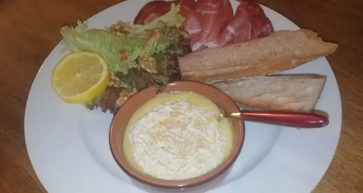 Un plat avec un fromage fondant, des tranches de jambon, de la salade, des noix, une tranche de citron et du pain. Une idée de recette amuse bouche facile sans cuisson.