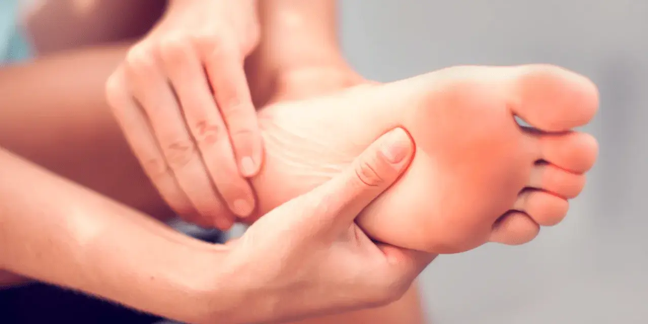 Hands massaging a foot, seeking aching feet remedy. The sole of the foot shows a slight red hue, indicating discomfort.