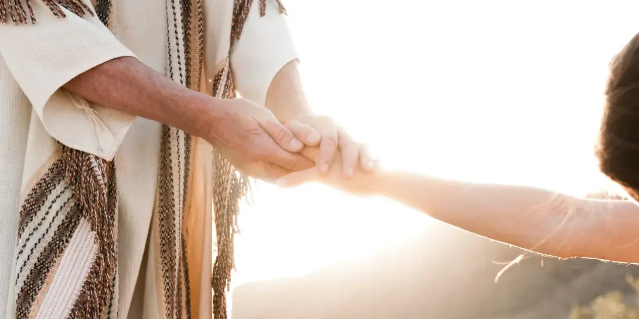 A person in a robe holds another's hand, symbolizing how to surrender to God through trust and guidance.