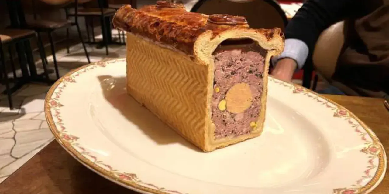 Un delicioso pâté de paques, un pastel de carne con un centro de foie gras, servido en un plato elegante.