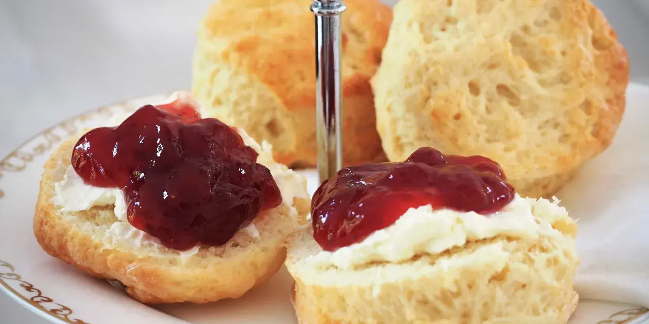 Was sind Scones? Köstliche, goldbraune Scones, bestrichen mit Clotted Cream und Marmelade, auf einer Etagere serviert. Ein Genuss für jeden Teeliebhaber.