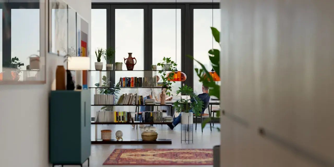 Un salón comedor dos ambientes con estanterías llenas de libros y plantas, y dos personas trabajando en una mesa.