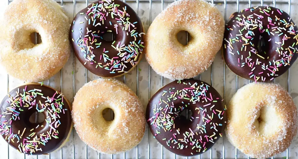 Åtta hemgjorda donuts, vissa med chokladglasyr och strössel, andra med socker. Perfekt för ett donuts recept!